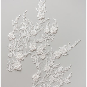 May include: White lace applique with a floral design. The lace features delicate branches with small white flowers and larger, more detailed flowers.