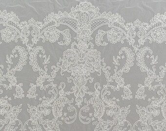 May include: White lace fabric with a delicate floral pattern. The lace has a scalloped edge and is perfect for adding a touch of elegance to any project.