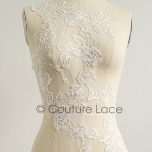 May include: White floral lace applique with delicate floral designs. The lace is on a mannequin and is perfect for adding a touch of elegance to any garment.