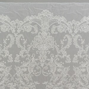 May include: White lace fabric with a delicate floral pattern. The lace has a scalloped edge and is perfect for adding a touch of elegance to any project.