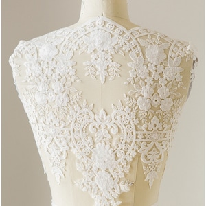 Peut inclure: Applique en dentelle blanche avec un motif floral. La dentelle est délicate et complexe, avec un bord festonné. Elle est parfaite pour ajouter une touche d'élégance à n'importe quel vêtement.