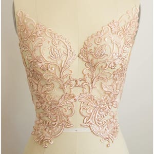 Puede incluir: Una delicada aplicación de encaje de color oro rosa con un diseño floral. El encaje es perfecto para añadir un toque de elegancia a cualquier prenda.