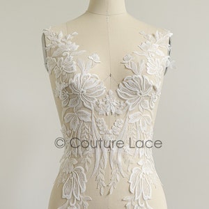 Puede incluir: Aplique de encaje floral blanco con delicados abalorios y una tela transparente. El encaje se muestra en un maniquí.