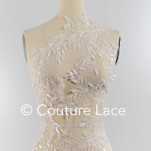 May include: White beaded lace applique with a leafy design. The lace is displayed on a dress form.