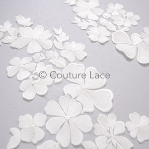 Op de afbeelding: Witte bloemenkant applique met delicate bloemmotieven. De kant is perfect om een ​​toets van elegantie toe te voegen aan elk project.