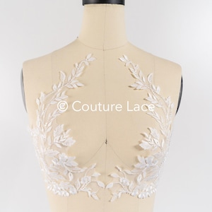 May include: White lace applique with a floral design. The lace is delicate and intricate, with small leaves and flowers. The applique is perfect for adding a touch of elegance to any garment.