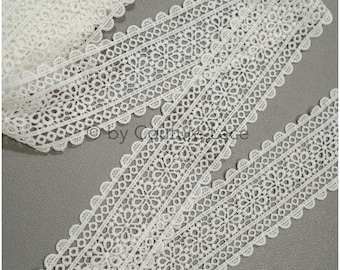 May include: White lace trim with a delicate floral pattern. The trim has a scalloped edge and is perfect for adding a touch of elegance to any project.