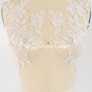 May include: White floral lace applique with intricate detailing. The design features delicate flowers and leaves, perfect for bridal or formal wear. The text "Couture Lace" is visible.
