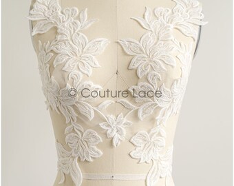 May include: White floral lace applique with a delicate design. The lace is on a white mannequin and is perfect for adding a touch of elegance to any garment.