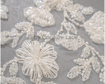 May include: White beaded lace trim with floral designs. The lace features delicate flowers and leaves, all made of small white beads. The lace is perfect for adding a touch of elegance to any project.