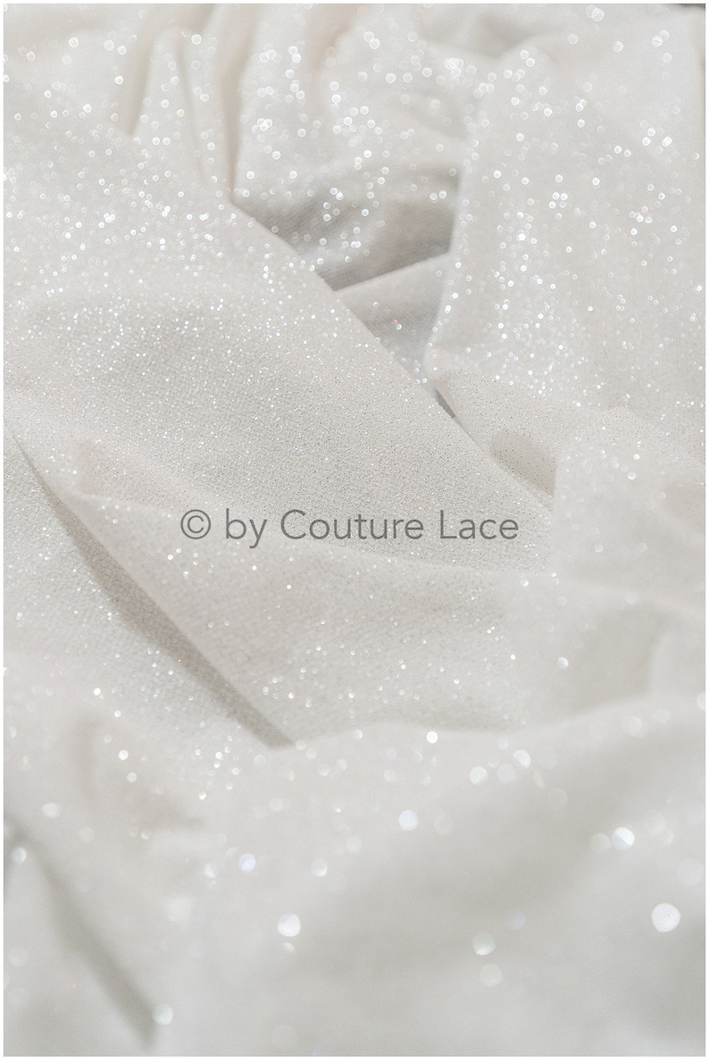 May include: White fabric with a sparkly, glittery texture. The fabric is folded and has a subtle sheen. The text "&copy; by Couture Lace" is visible in the lower center of the image.