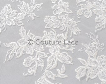 Puede incluir: Tela de encaje floral blanca con un patrón delicado. El encaje está sobre un fondo de malla transparente. El texto "Couture Lace" es visible en el centro de la imagen.