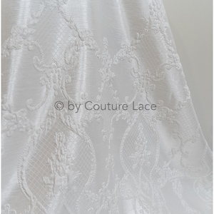 May include: White fabric with an embossed floral pattern. The fabric has a subtle sheen and a delicate, intricate design. &copy; by Couture Lace