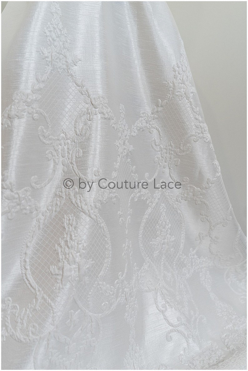 May include: White fabric with an embossed floral pattern. The fabric has a subtle sheen and a delicate, intricate design. &copy; by Couture Lace