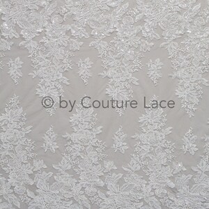 May include: White floral lace fabric with a delicate pattern and small sequins. The fabric is sheer and has a soft, flowing texture. &copy; by Couture Lace