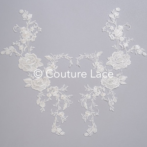 May include: Two white lace appliques with floral designs, featuring delicate vines and roses. The appliques are perfect for adding a touch of elegance to wedding dresses, bridal accessories, or other craft projects.