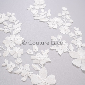 Op de afbeelding: Witte bloemenkant met een delicaat ontwerp. De kant heeft kleine bloemen en bladeren, perfect om een ​​toets van elegantie aan elk project toe te voegen.