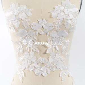 Pode incluir: Aplique de renda branca floral com detalhes de contas. A renda é delicada e intrincada, com um padrão floral. O aplique é perfeito para adicionar um toque de elegância a qualquer peça de roupa.
