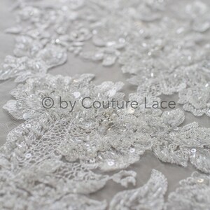 May include: White beaded lace fabric with a floral design. The lace is delicate and intricate, with small beads and sequins scattered throughout. The fabric is perfect for wedding dresses, bridal accessories, and other special occasion garments.