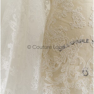 May include: White lace fabric with a floral pattern. The lace is delicate and intricate, with a soft, flowing texture. The fabric is shown draped over a dress form.