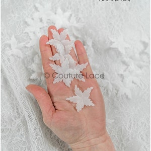 May include: Four white lace flower appliques, each measuring approximately 4 cm in diameter. The appliques are in the shape of a five-pointed star with a delicate, intricate design. The appliques are shown on a hand against a white lace background. FL-019 (ø 4cm)