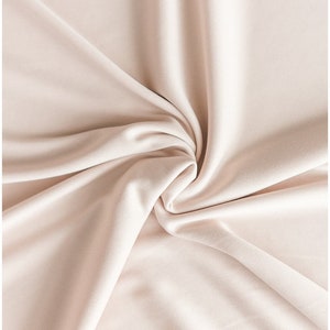 May include: A close-up of a smooth, pale pink fabric with soft folds and wrinkles. The fabric is draped and gathered in a swirling pattern, creating a luxurious and elegant texture.