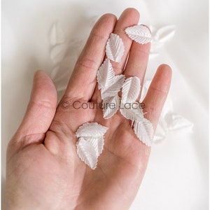 May include: A hand holding a handful of white fabric leaves. The leaves are delicate and have a slightly textured surface.