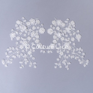 May include: Two white floral lace appliques with delicate flowers and leaves. The appliques are perfect for adding a touch of elegance to any project.
