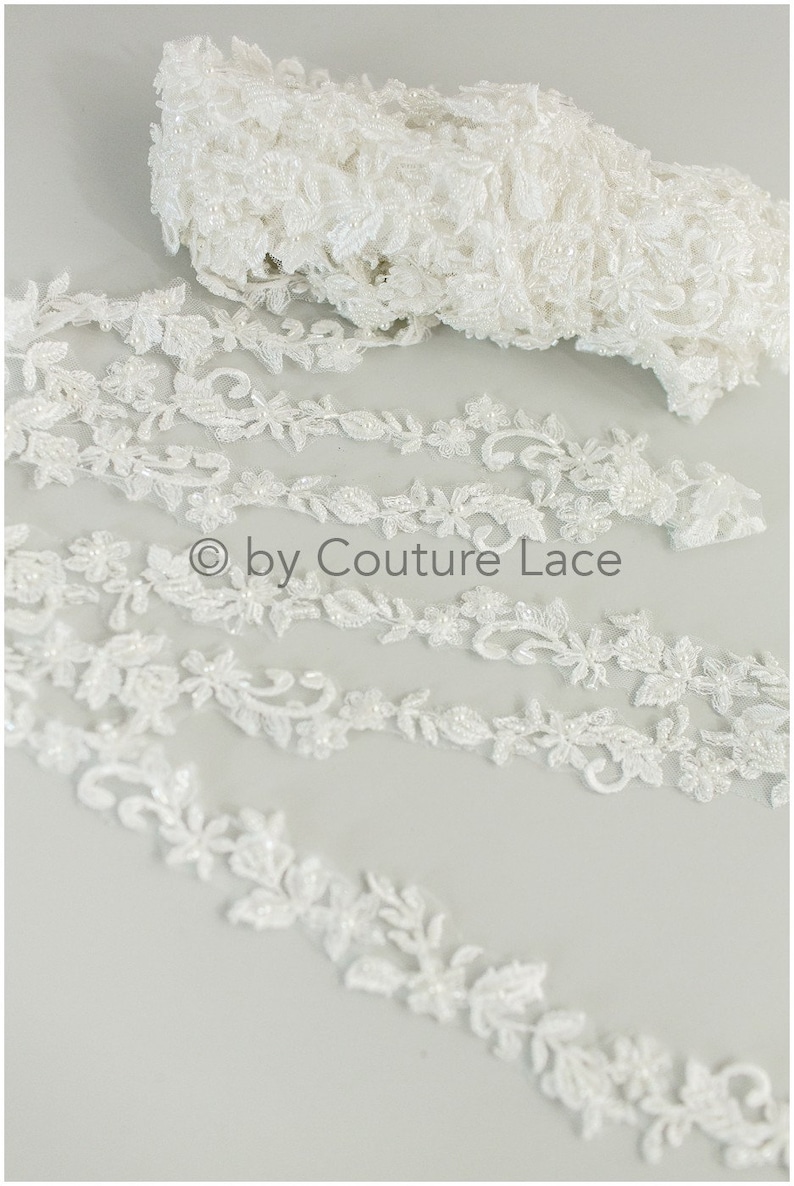 May include: White beaded lace trim with a floral design. The lace is delicate and intricate, with small beads scattered throughout. &copy; by Couture Lace