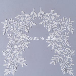 May include: White lace trim with a delicate floral design. The lace is arranged in a curved shape, resembling a garland or wreath. The lace is on a light purple background.