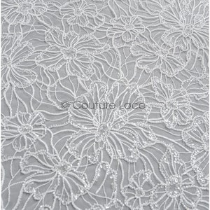 Pu&ograve; includere: Tessuto di pizzo floreale bianco con un delicato motivo di fiori e paillettes. Il tessuto ha una texture morbida e fluida ed &egrave; perfetto per creare abiti o accessori eleganti.