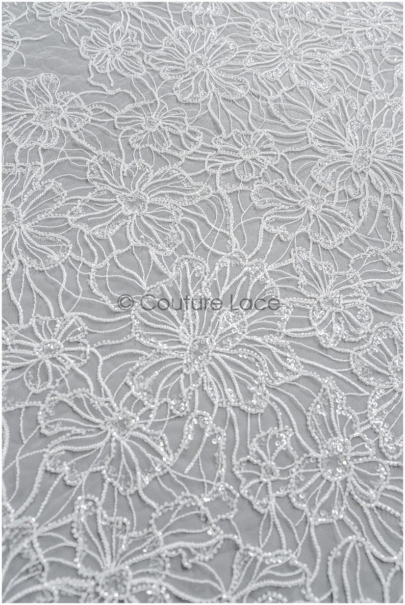 Pu&ograve; includere: Tessuto di pizzo floreale bianco con un delicato motivo di fiori e paillettes. Il tessuto ha una texture morbida e fluida ed &egrave; perfetto per creare abiti o accessori eleganti.