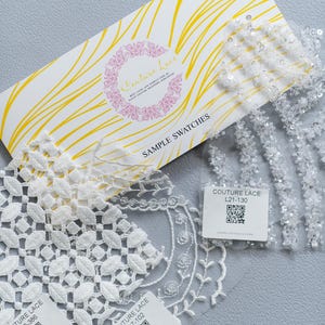 Peut inclure: Trois échantillons de dentelle blanche sur fond blanc. Chaque échantillon est accompagné d'une étiquette blanche avec le texte "Couture Lace" et un code unique. Les codes sont L20-386, L17-102 et L21-130. Chaque étiquette comporte également un code QR.