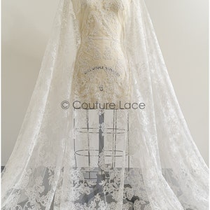 May include: White lace fabric with a delicate floral pattern. The lace is on a sheer tulle backing. The fabric is draped over a dress form. The text "Couture Lace" is visible in the image.