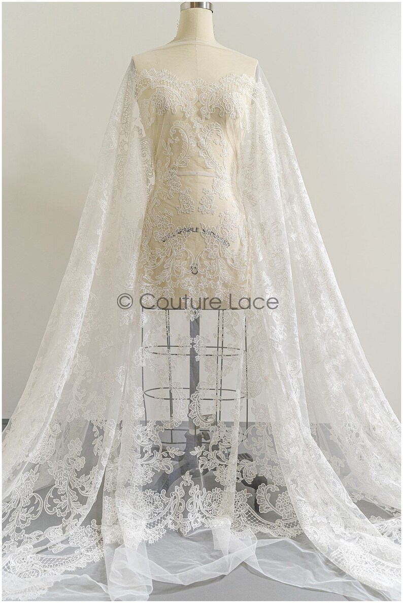 May include: White lace fabric with a delicate floral pattern. The lace is on a sheer tulle backing. The fabric is draped over a dress form. The text "Couture Lace" is visible in the image.
