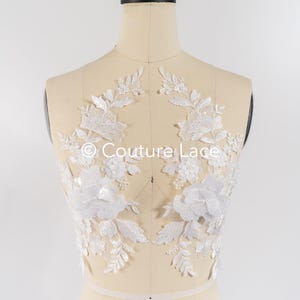 May include: White floral lace applique with delicate leaves and beaded accents. The lace is on a mannequin and is ready to be sewn onto a garment.