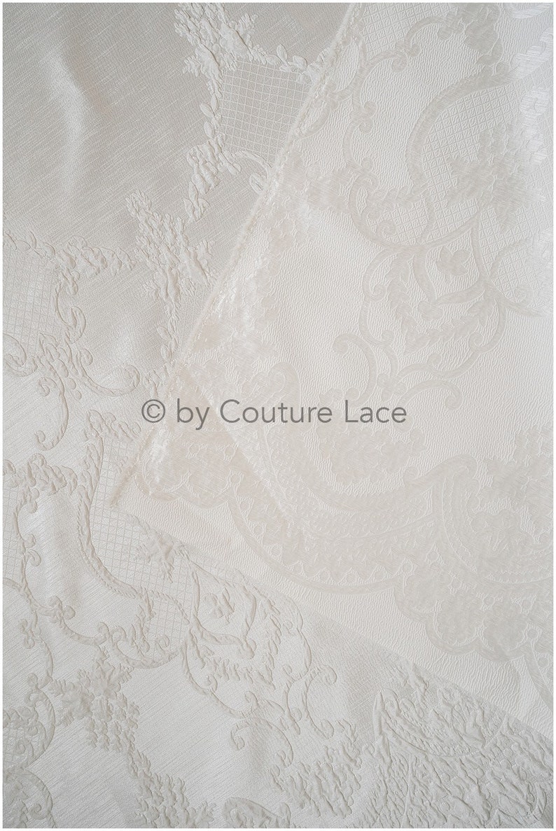 May include: White fabric with a raised, embossed pattern of a floral design. The fabric is folded in half, and the text "&copy; by Couture Lace" is visible in the center of the image.