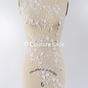 May include: White floral lace applique with delicate beading and a vine design. The lace is displayed on a dress form.