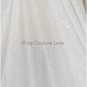 May include: White sparkly tulle fabric with a subtle sheen. The fabric is lightweight and has a delicate texture. &copy; by Couture Lace