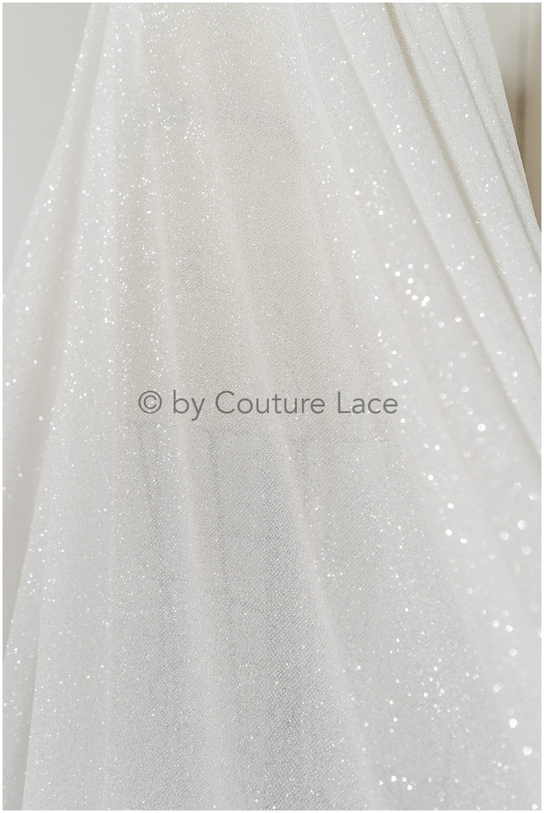 May include: White sparkly tulle fabric with a subtle sheen. The fabric is lightweight and has a delicate texture. &copy; by Couture Lace