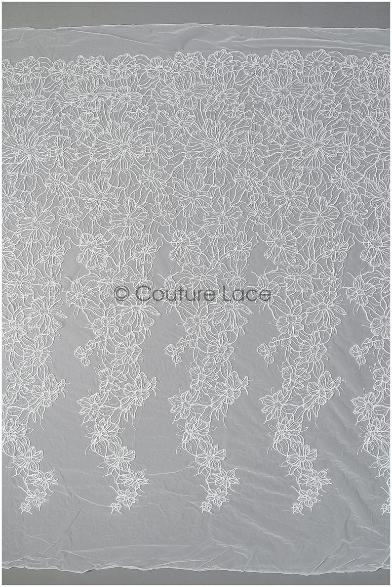 Pu&ograve; includere: Tessuto di pizzo floreale bianco con un design delicato e intricato. Il pizzo presenta un motivo ripetitivo di piccoli fiori e foglie.