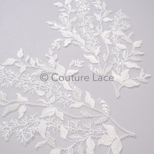 May include: White lace fabric with a delicate floral design and beaded accents. The fabric features a repeating pattern of leaves and vines.