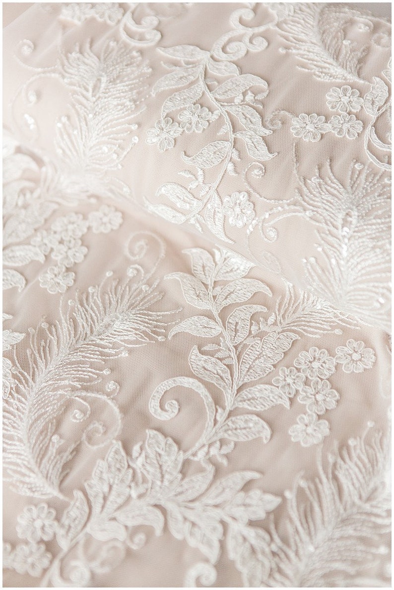 May include: Close-up of delicate white lace fabric with a floral pattern. The lace features intricate designs of leaves, flowers, and swirls.