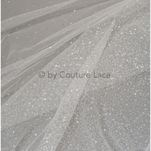 Peut inclure: Tulle blanc avec des paillettes argentées éparses. Le tissu est transparent et a une texture délicate. © by Couture Lace