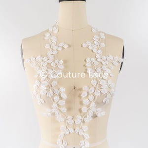 Può includere: Applique in pizzo bianco con un motivo a foglie. L'applique è su un manichino bianco. Il testo "Couture Lace" è visibile sull'applique.