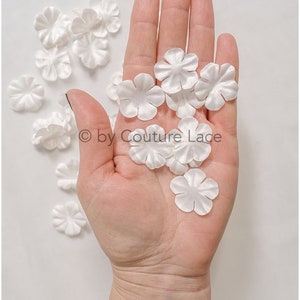 Könnte beinhalten: Eine Hand hält einen Haufen weißer Satin-Blütenblätter. Die Blütenblätter sind weich und zart und eignen sich perfekt, um jedem Bastelprojekt einen Hauch von Eleganz zu verleihen.