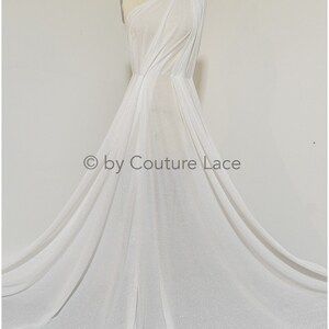 May include: White sparkly fabric draped on a dress form. The fabric is sheer and has a subtle shimmer. The fabric is shown in a flowing, draped style. &copy; by Couture Lace