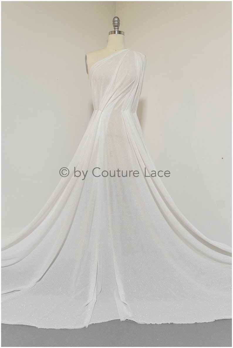 May include: White sparkly fabric draped on a dress form. The fabric is sheer and has a subtle shimmer. The fabric is shown in a flowing, draped style. &copy; by Couture Lace