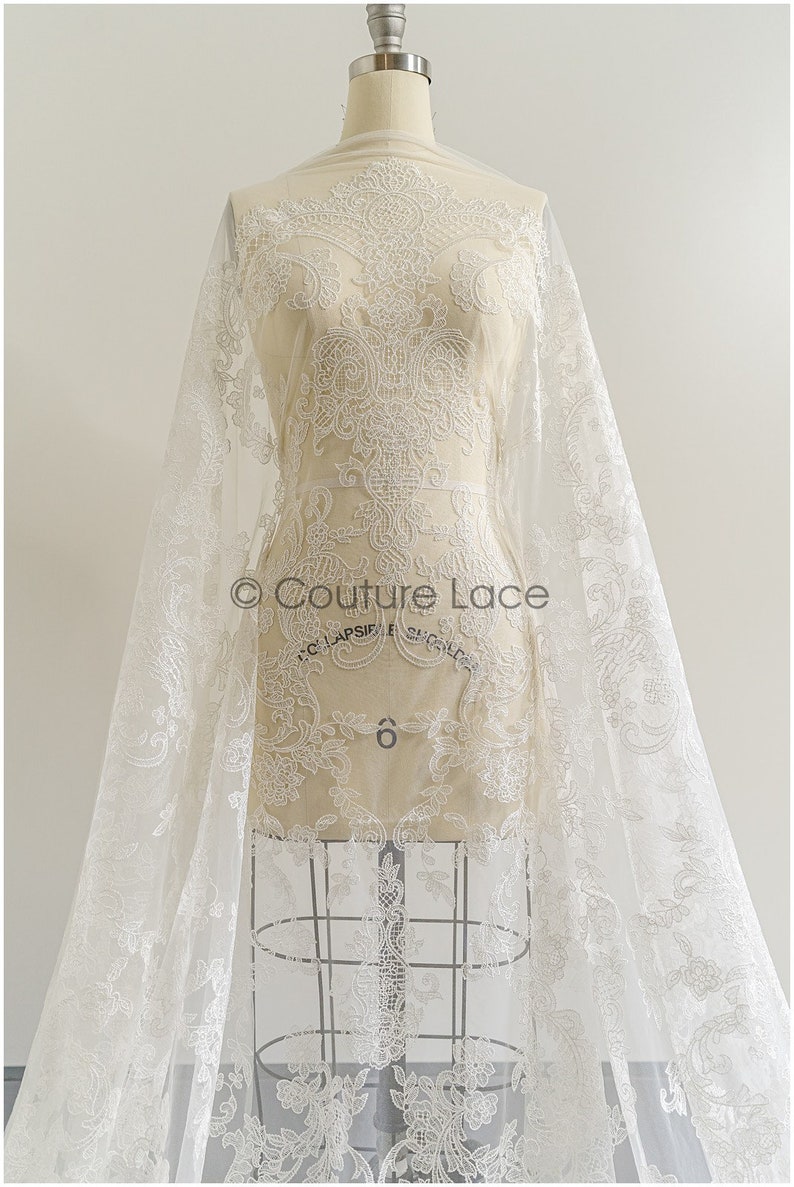 May include: White lace fabric with a delicate floral pattern. The lace is displayed on a dress form and has a sheer, lightweight texture.
