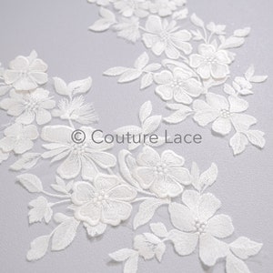 Op de afbeelding: Witte bloemvormige kant applique met delicate bloemen en bladeren. Deze kant trim is perfect om een ​​toets van elegantie toe te voegen aan elk project.